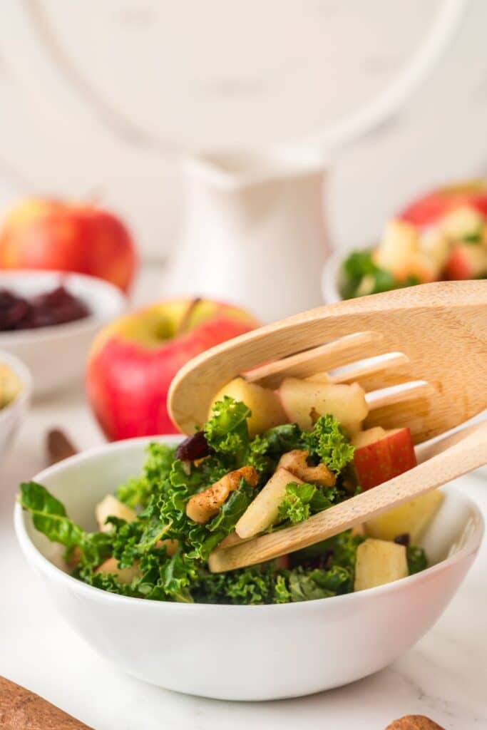 Serving Kale Apple Salad with 2 serving spoons into a small white bowl.