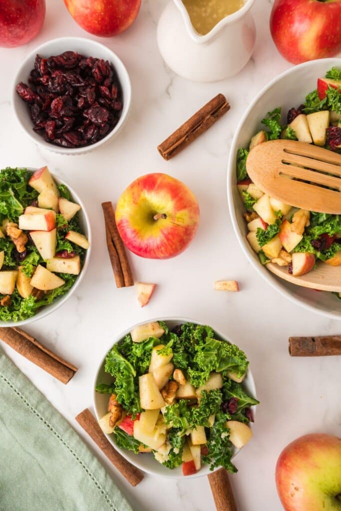 Multiple bowls, and serving bowl, of Kale Apple Salad and ingredients used in it.