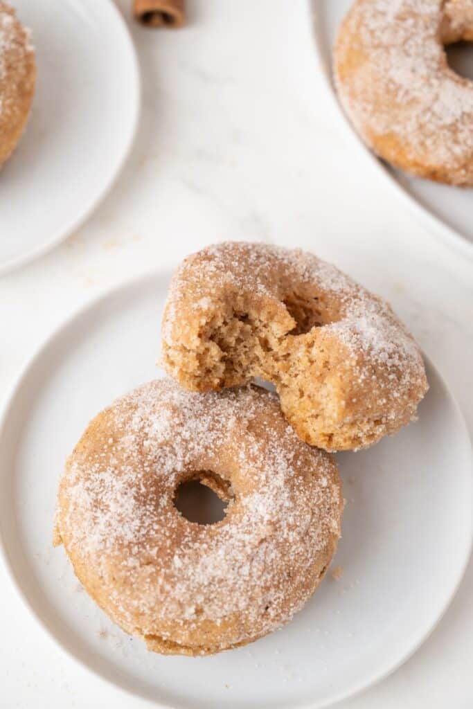 Vegan Apple Cider Donuts on white plate with a bite taken out of 1 of the two donuts shown.